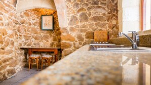 A stone-walled kitchen with a granite countertop, a sink, and two wicker chairs. - TA Filomena (Xaghra)