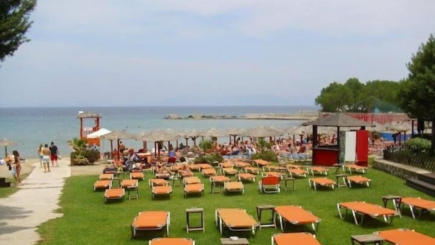 Ein Strandresort mit Liegestühlen auf einer Rasenfläche, einer Pier, die sich ins Meer erstreckt, und einigen Personen, die auf dem Weg entlanggehen.