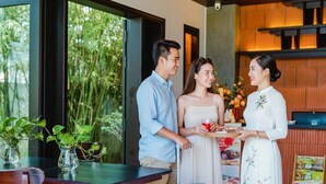 A modern hotel room with a large window, a dining table with a vase of plants, and a suitcase. - Én Retreat Hoi An (Da Nang)