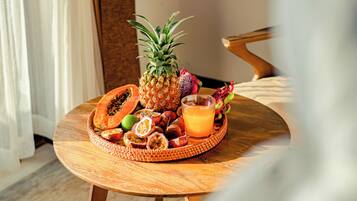 A wooden table with a fruit and juice tray, a pineapple, papaya, passion fruit, dragon fruit, and a glass of orange juice.