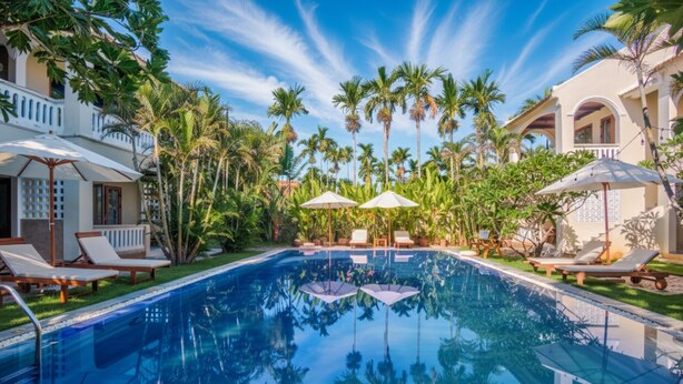 A pool surrounded by palm trees and lounge chairs. - Én Retreat Hoi An (Da Nang)