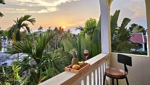 A balcony with a view of a sunset, a wooden crate with fruits and a glass of red wine, and a chair. - Én Retreat Hoi An (Da Nang)