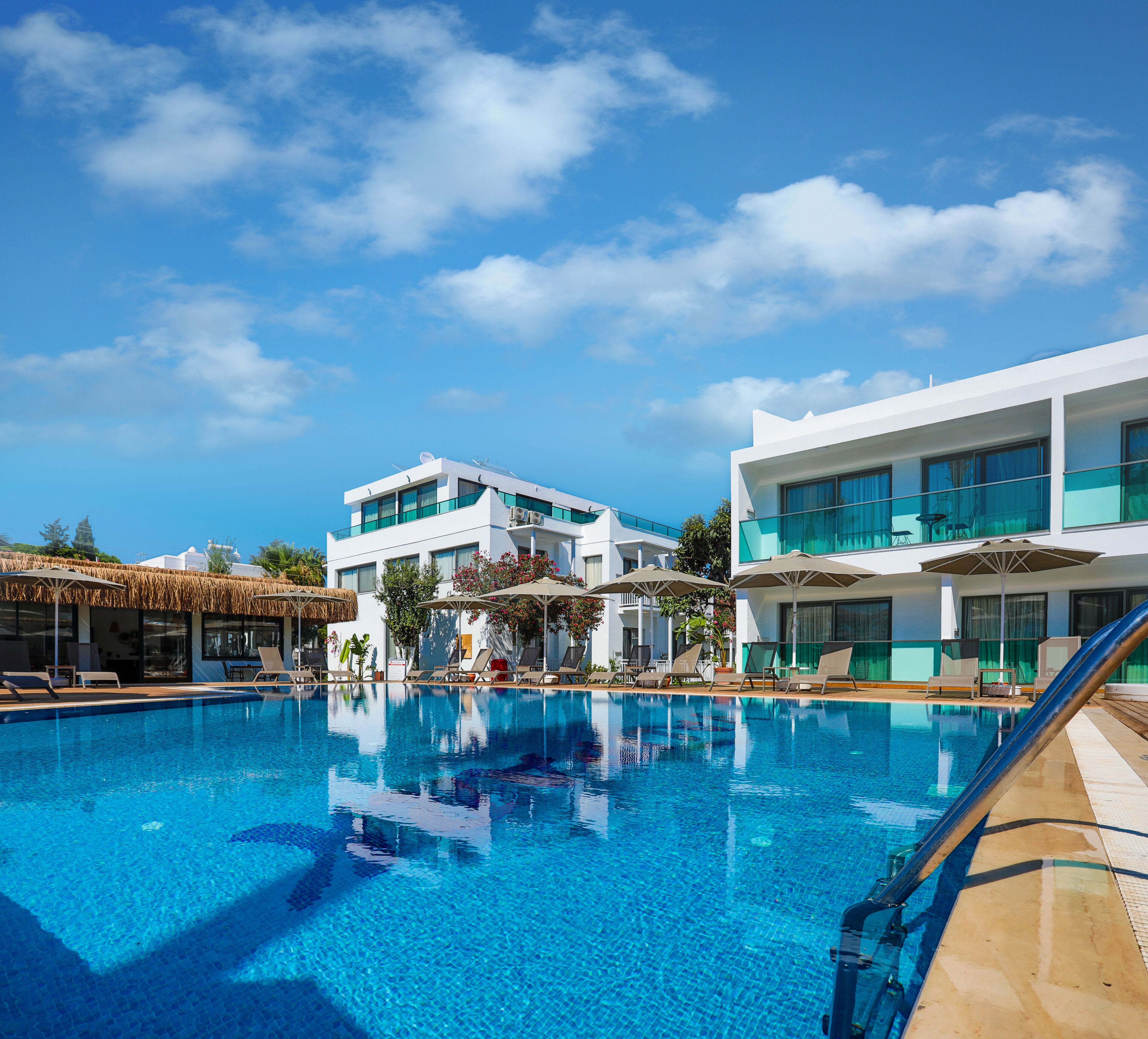 A swimming pool with lounge chairs and umbrellas, surrounded by modern buildings with large windows and balconies.