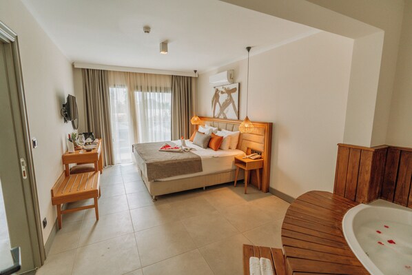 Habitación de hotel con cama, mesitas de noche, escritorio, silla, baño con bañera y un amplio ventanal con cortinas.