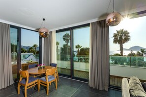 Una habitación moderna con una mesa de comedor, sillas y un sofá. Cuenta con ventanas grandes que ofrecen vistas a palmeras y montañas.