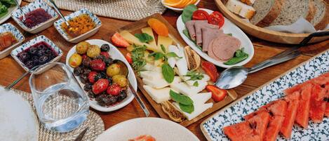 Een tafel met diverse etenswaren, zoals brood, kaas, tomaten en stukken watermeloen.