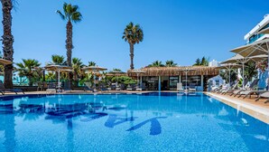 Una piscina con sillas de descanso y sombrillas, rodeada de palmeras.