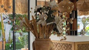 Una mesa redonda de vidrio con base de madera, un florero de madera con flores secas y una cocina moderna al fondo.