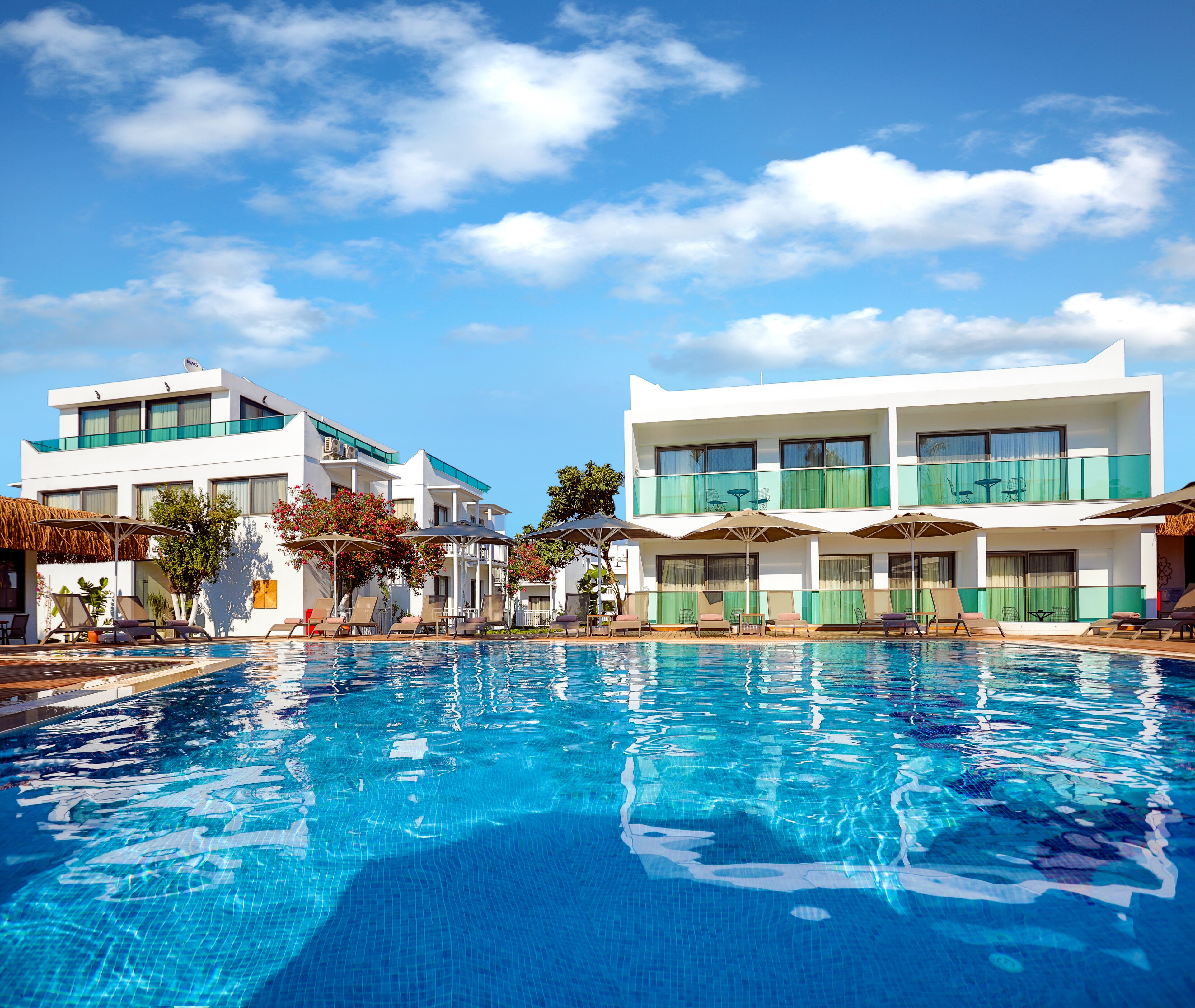 Un hotel moderno con piscina, varios balcones y zonas de estar al aire libre.