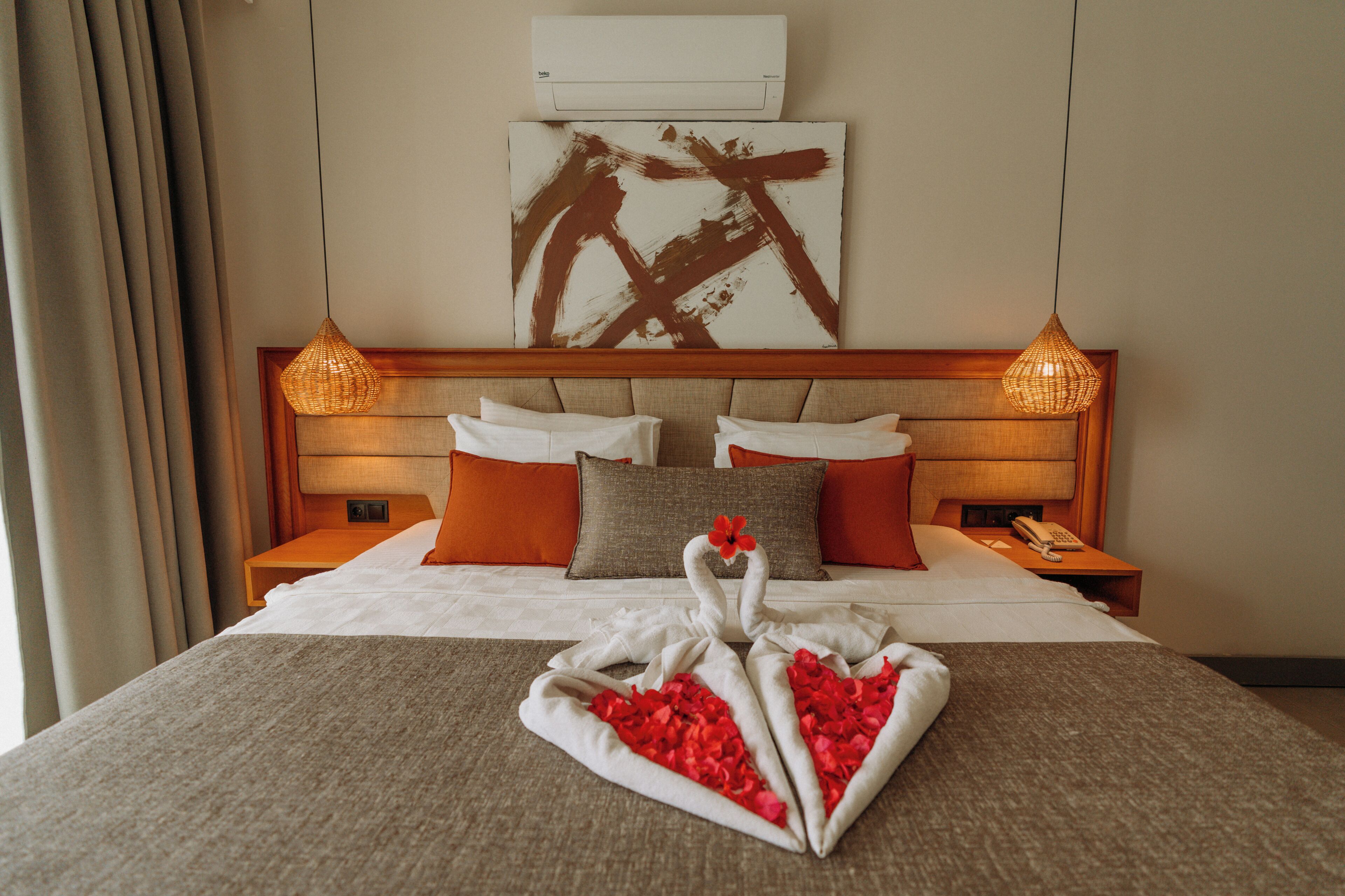 Une chambre d’hôtel avec un lit, des oreillers, une œuvre d’art murale et un cygne décoratif fait de serviettes et de pétales de rose.
