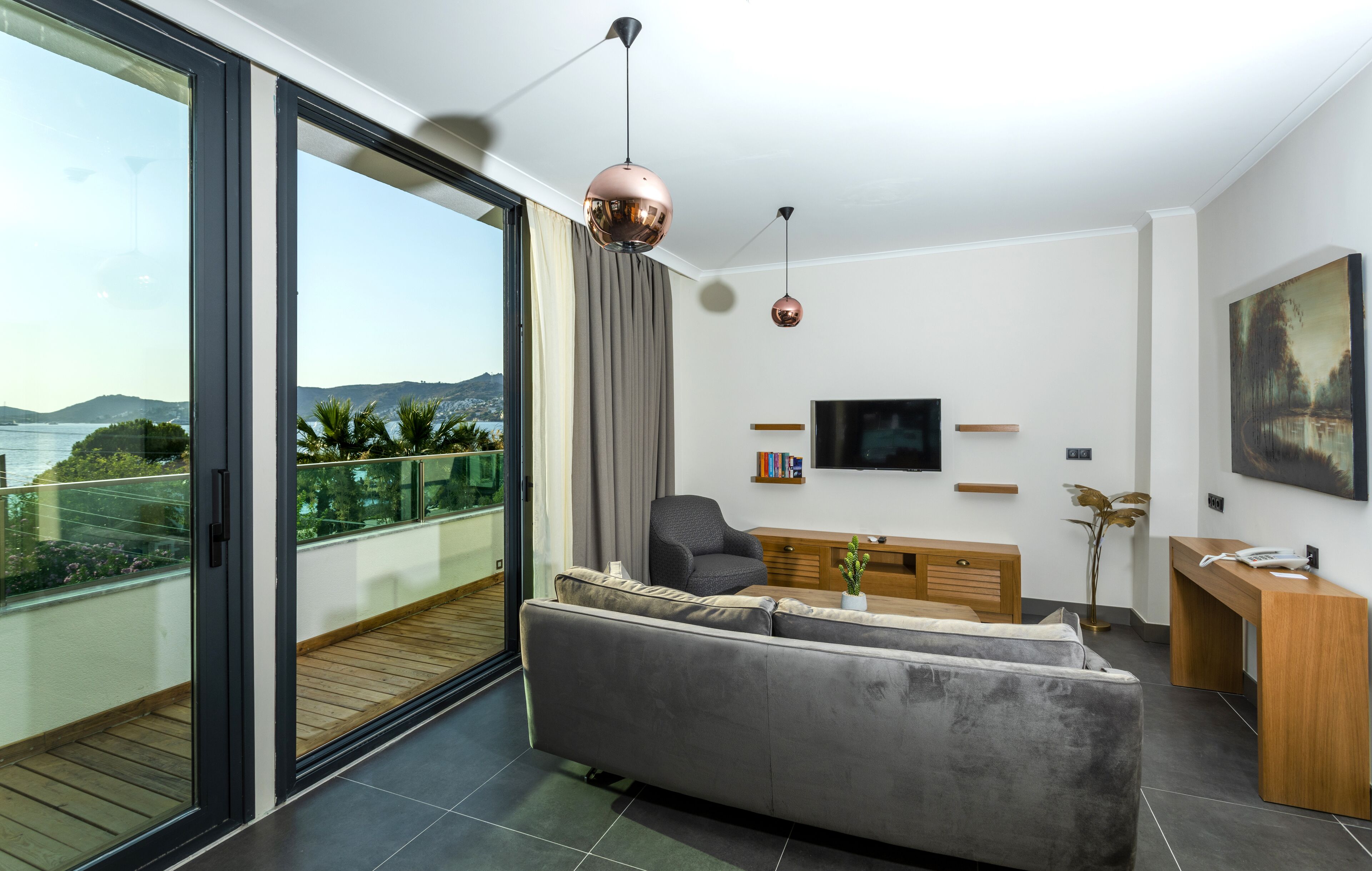 A modern living room with a grey sofa, a wooden desk, and a TV on the wall.