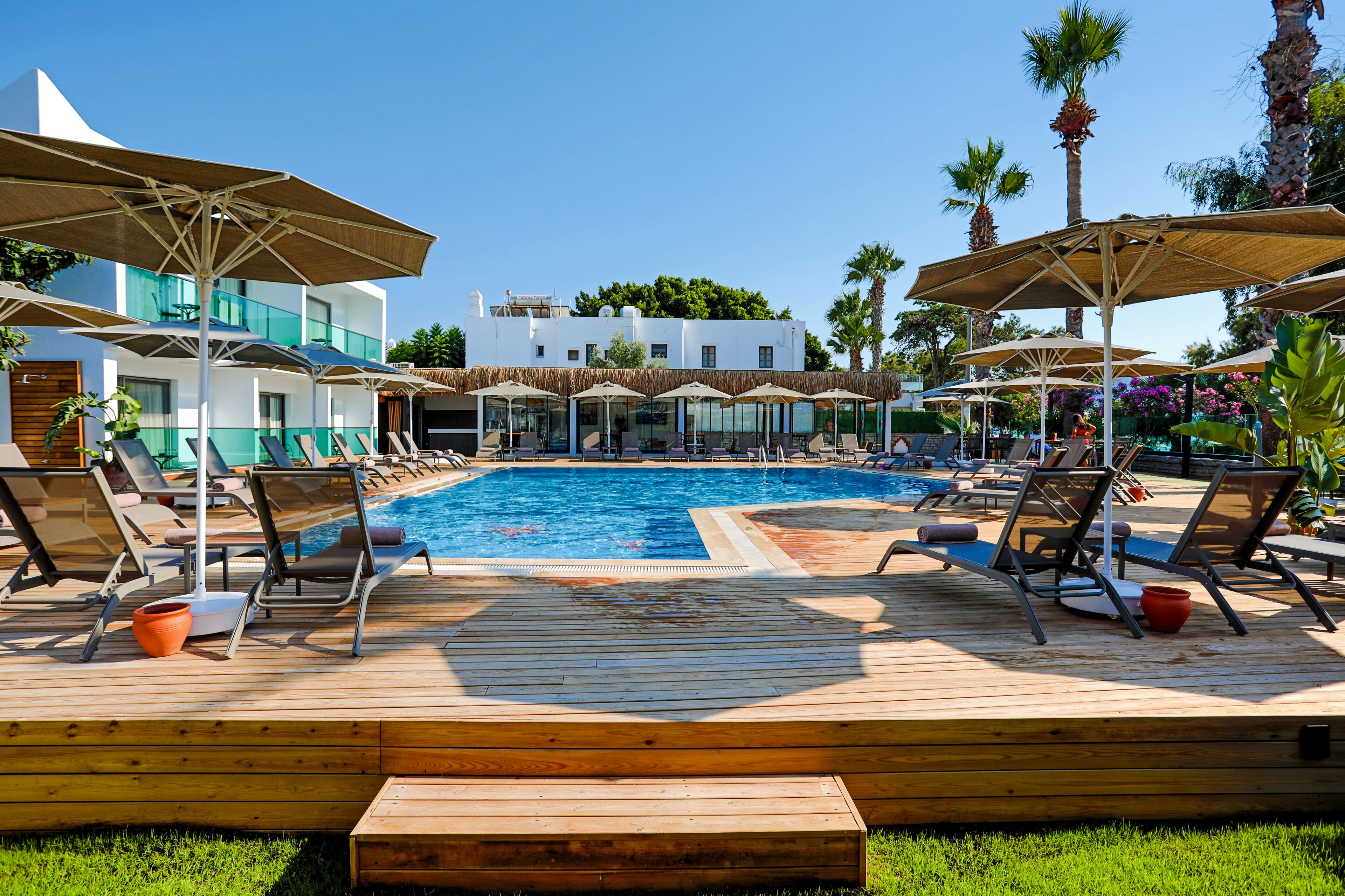 Zona de piscina con sillones, sombrillas y vista despejada de un edificio al fondo.