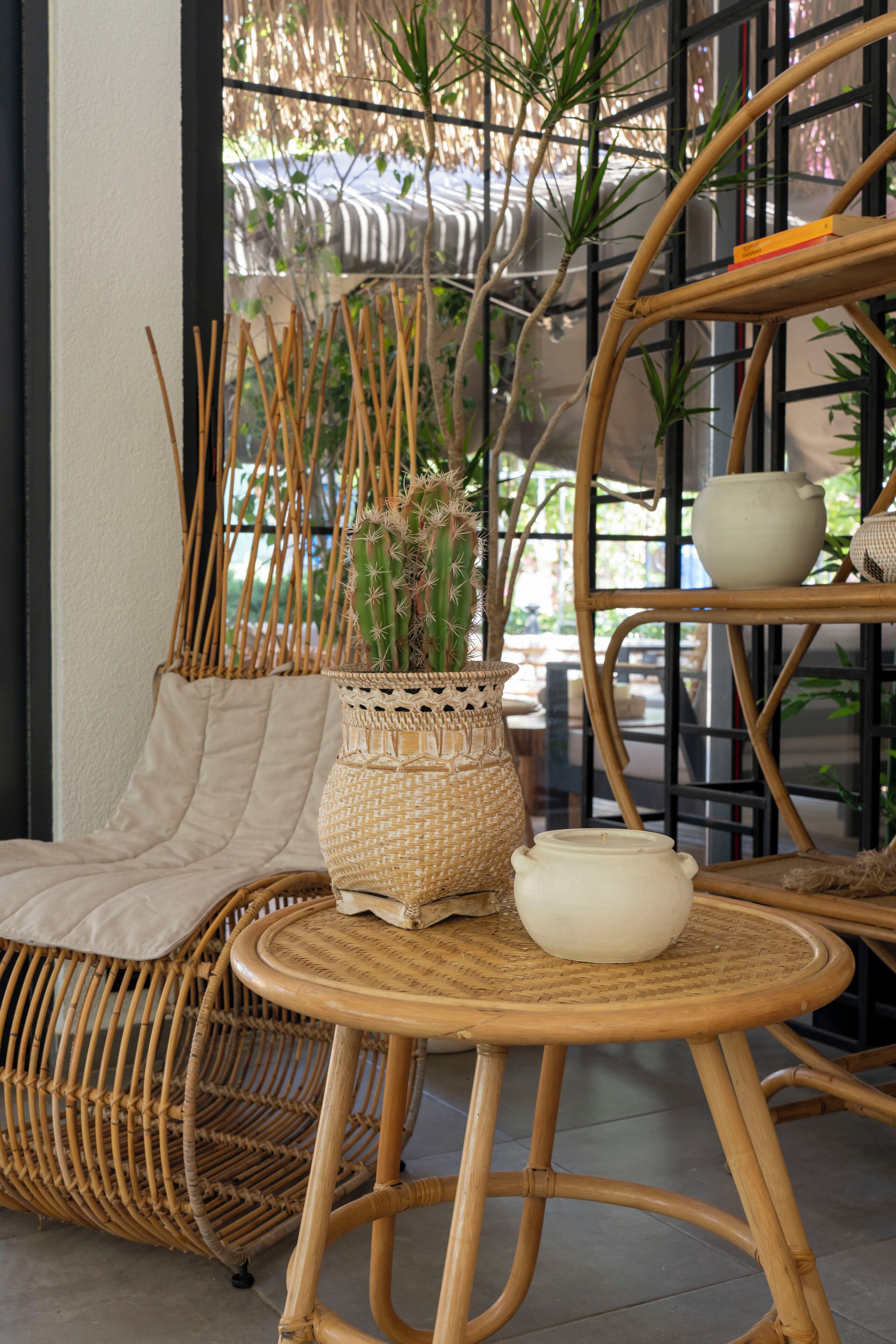 A wicker chair with a cushion, a small round table with a bowl, and a woven basket with a plant.