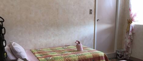 A double bed with pink and green floral bedding, a framed picture on the wall, and a door with a no-smoking sign.
