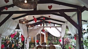 An outdoor dining area with tables and chairs, covered by a canopy with heart-shaped decorations.