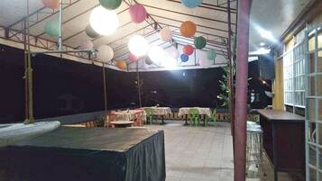 An indoor venue with tables and chairs arranged for dining or events, under a roof with hanging paper lanterns.