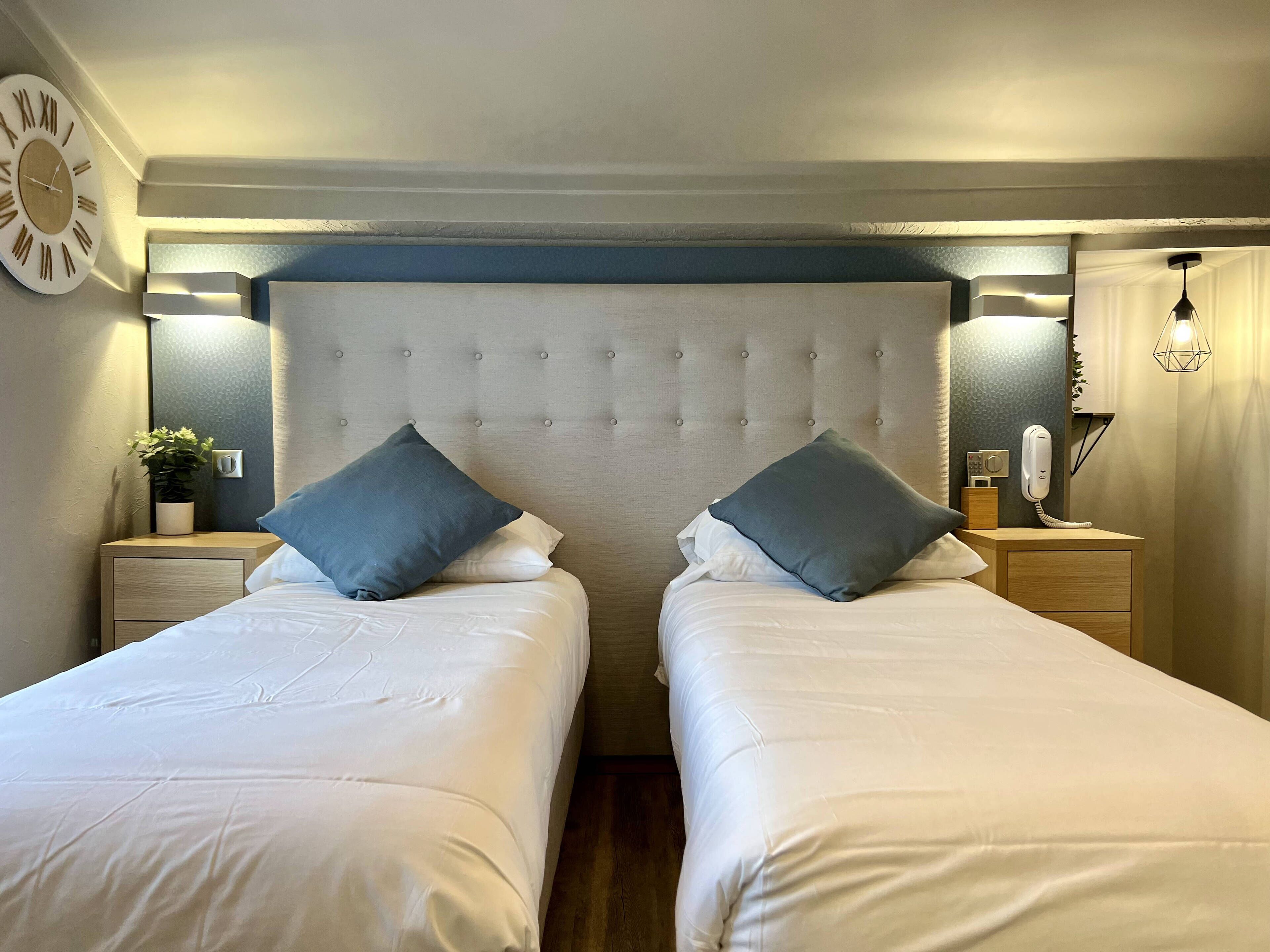 Een hotelkamer met twee enkele bedden, een gestoffeerd hoofdeinde, nachtkastjes met lampen, een wandklok en een telefoon.