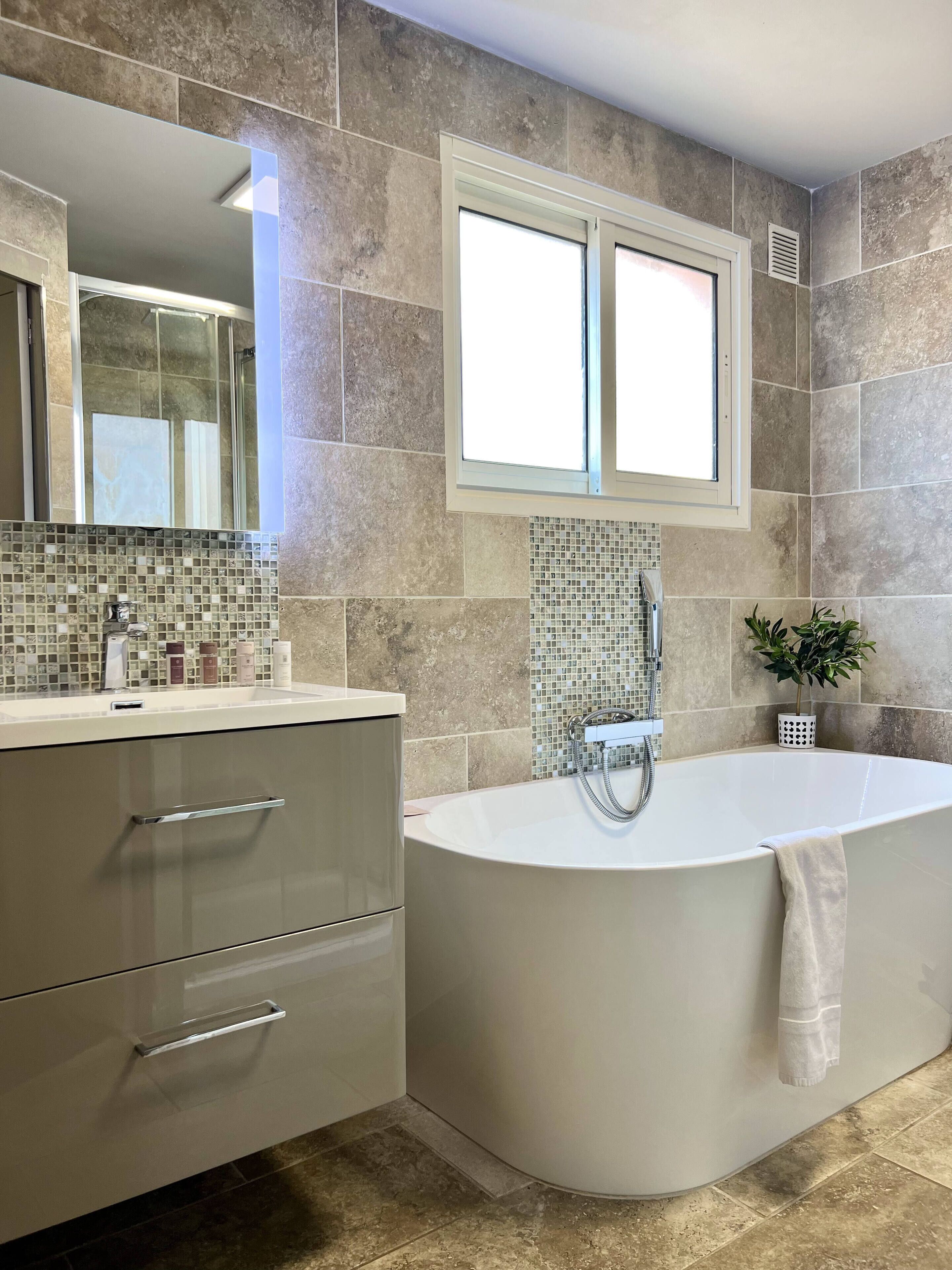 A modern bathroom with a freestanding bathtub, a large mirror, and a tiled backsplash.