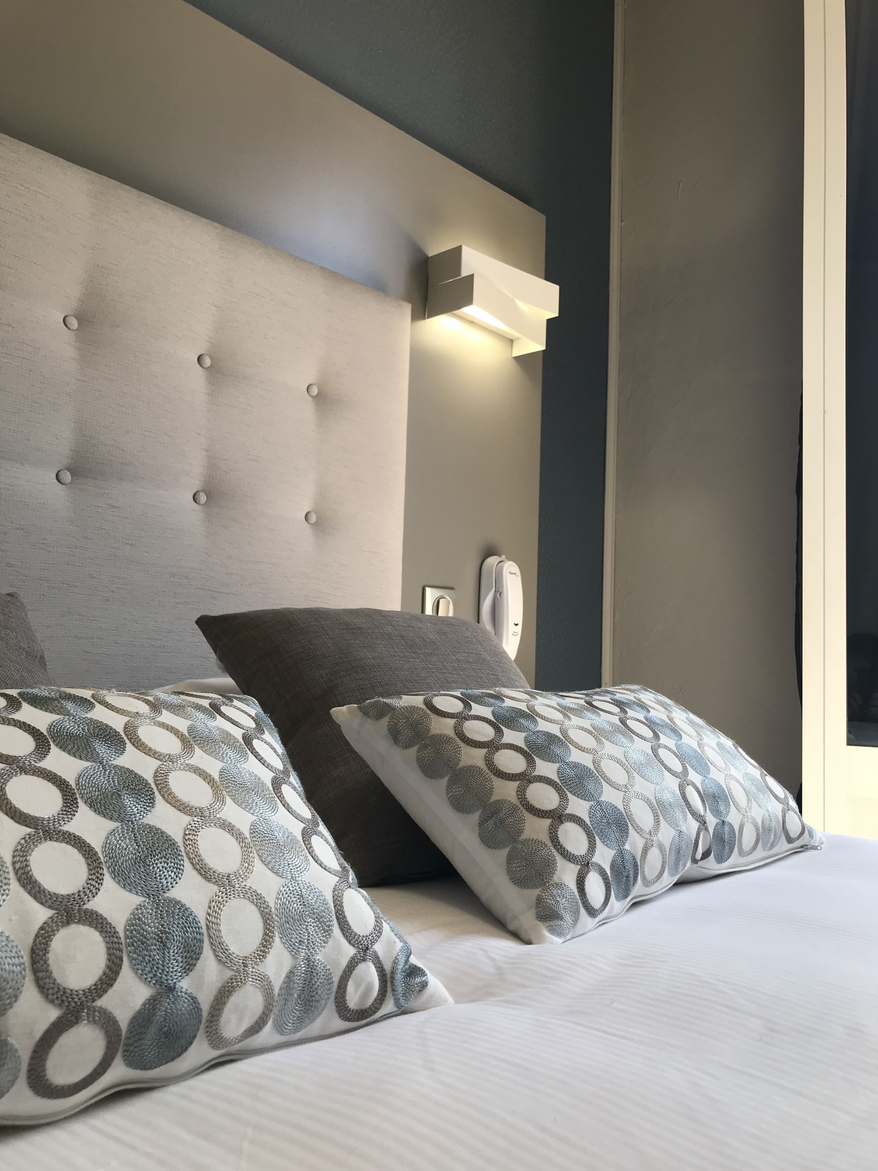 A modern bedroom with a tufted headboard, two patterned pillows, and a bedside table with a lamp.