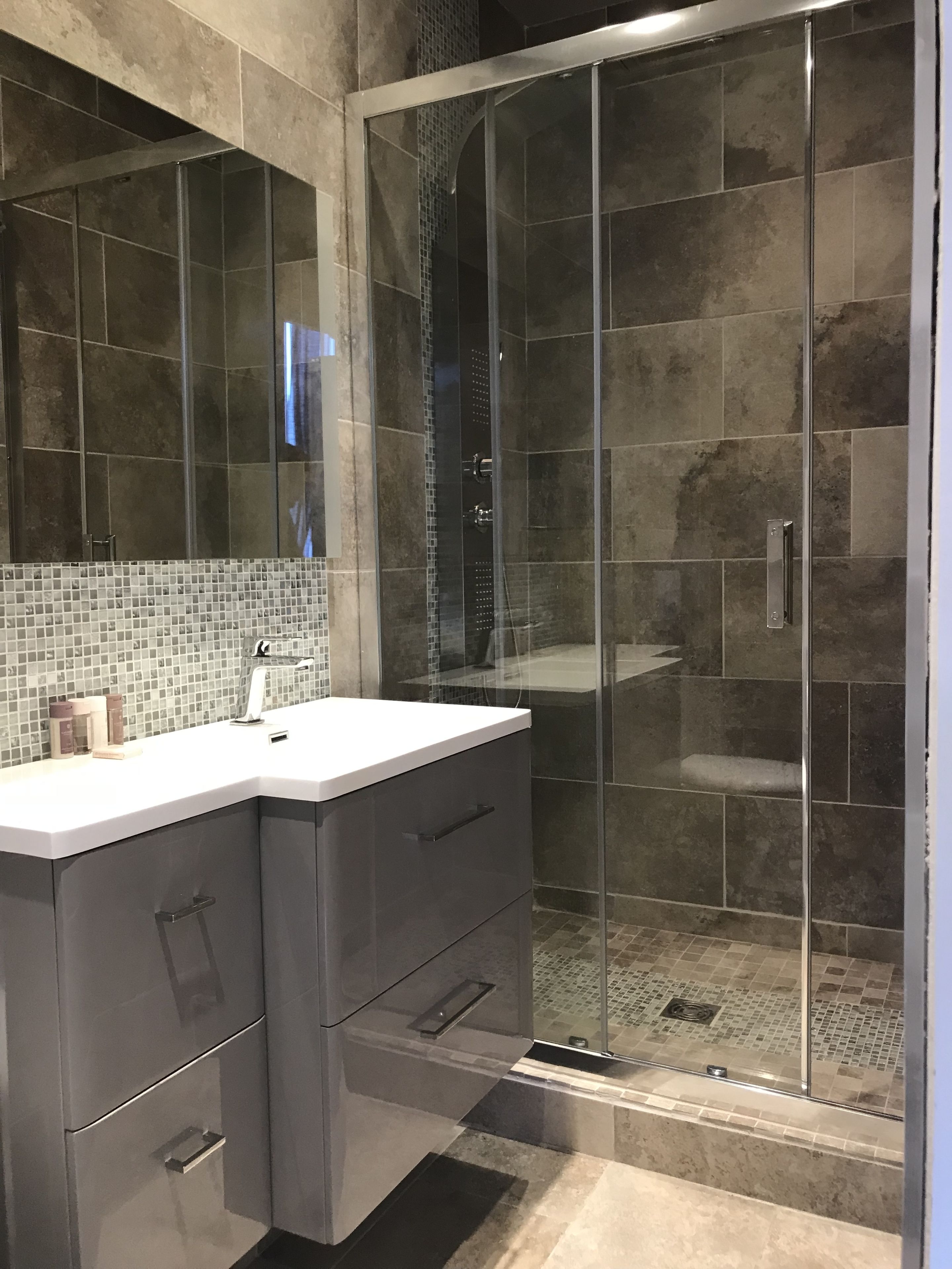 A modern bathroom with a glass-enclosed shower, a white sink, and dark-toned cabinets.