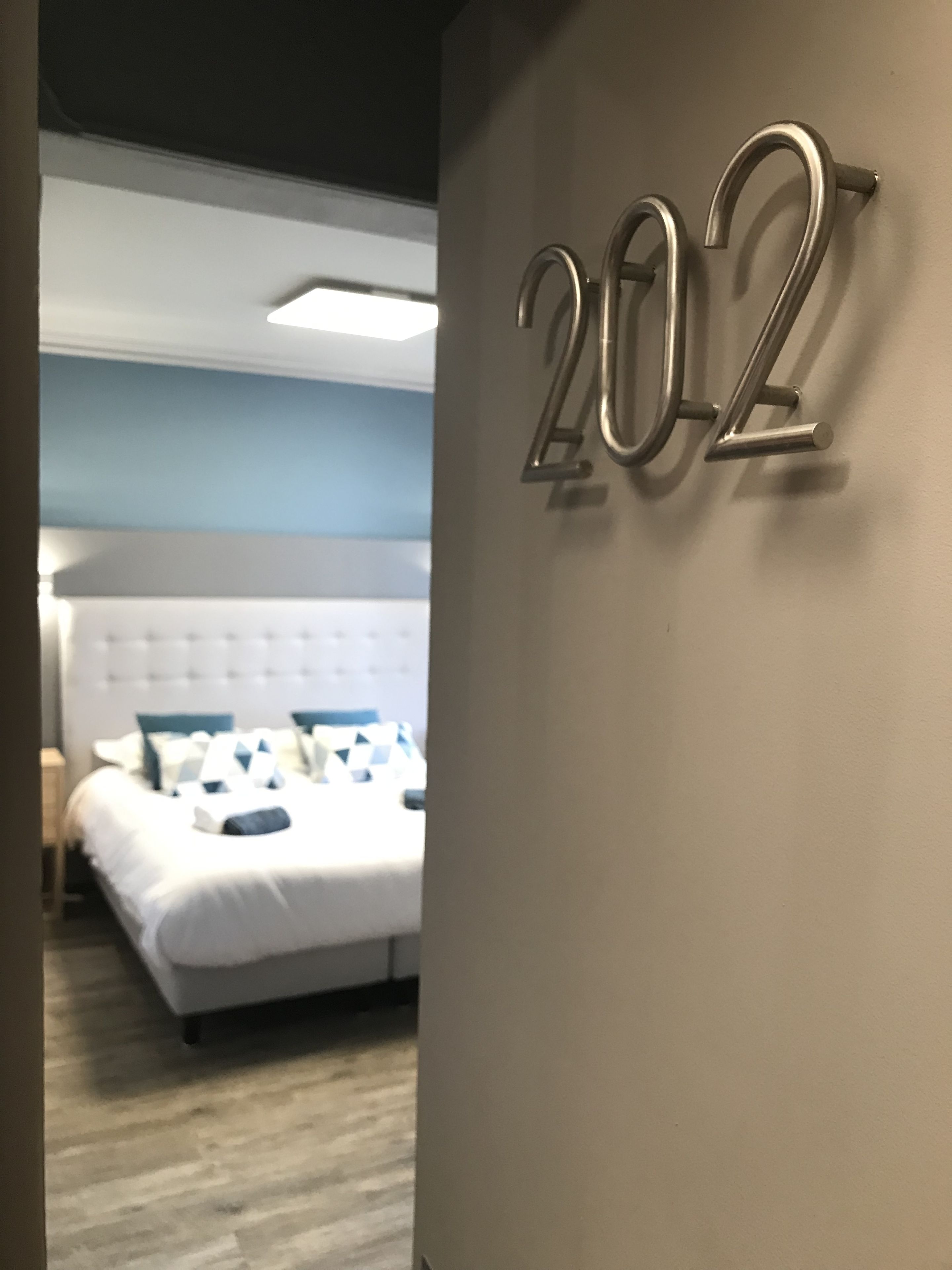 Een hotelkamer met een groot bed, een wandgemonteerd nummerbord en een zichtbare deur.