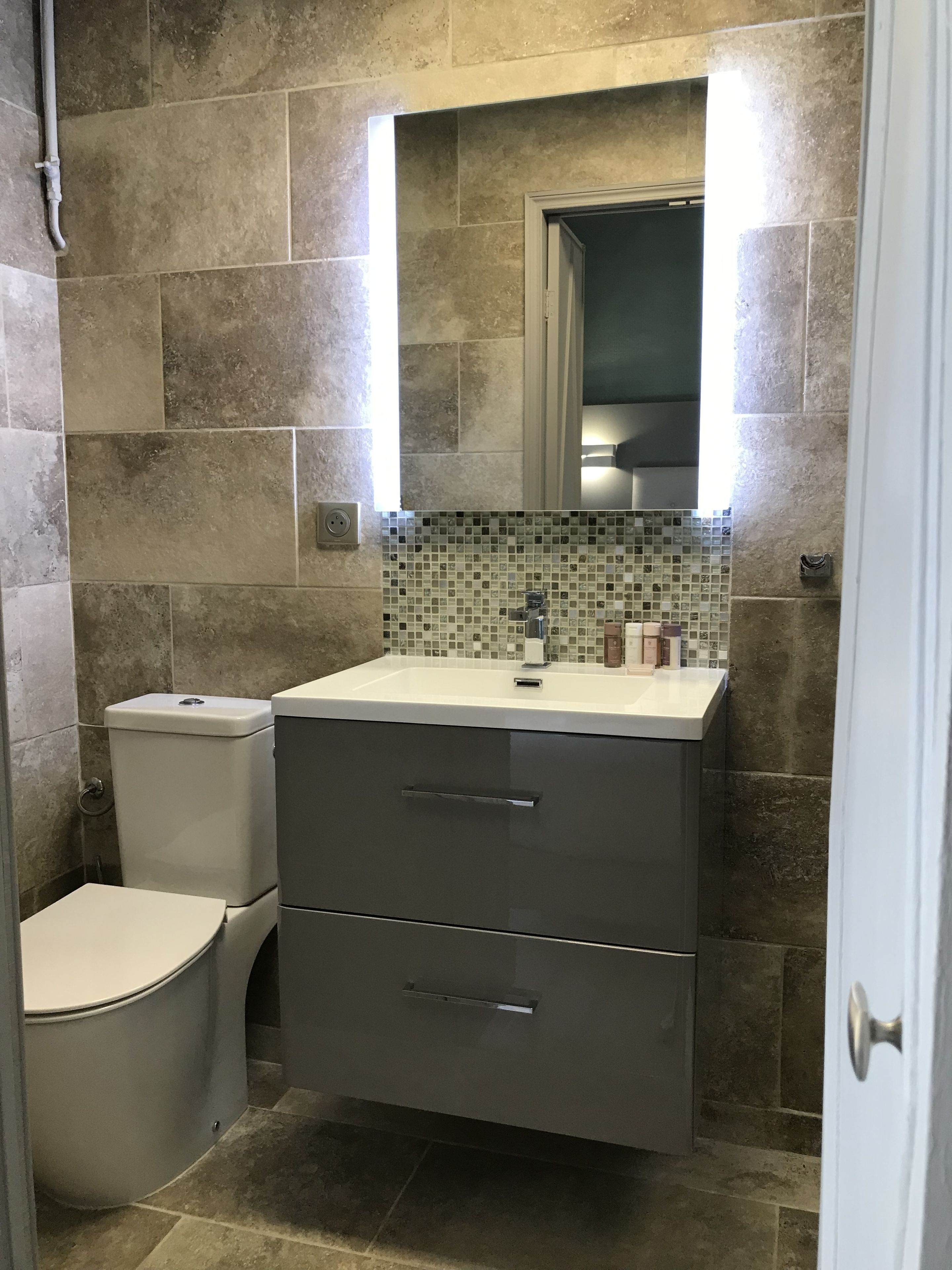 A bathroom with a toilet, a sink with a mirror, and tiled walls.