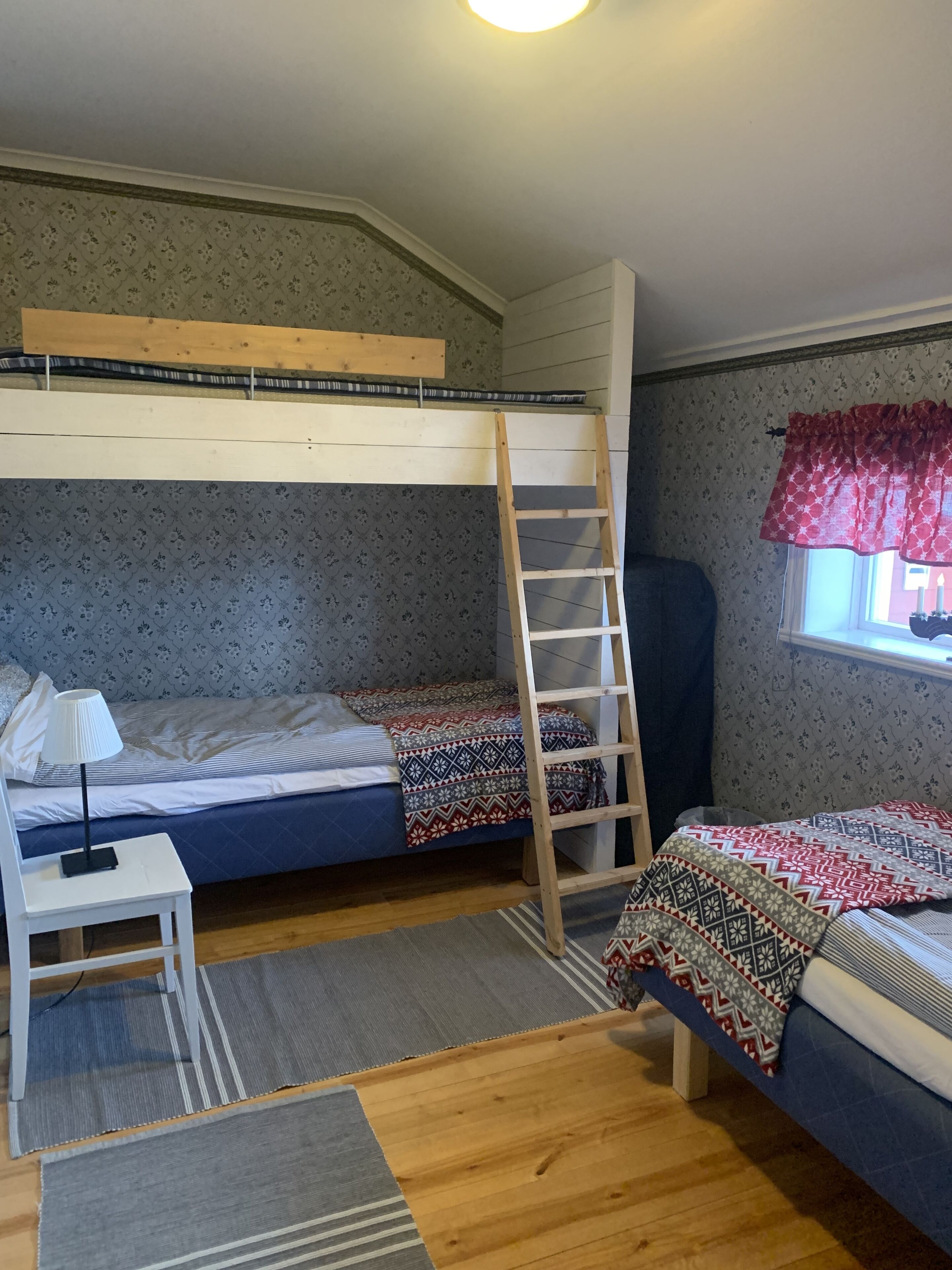 Habitación tipo dormitorio con literas, un escritorio, una silla, una escalera y una ventana con cortinas.