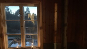 A cozy cabin interior with a wooden interior, a window with a view of a snowy landscape, and a wood-burning stove. - Chinova Mötesgård (Jarvso)