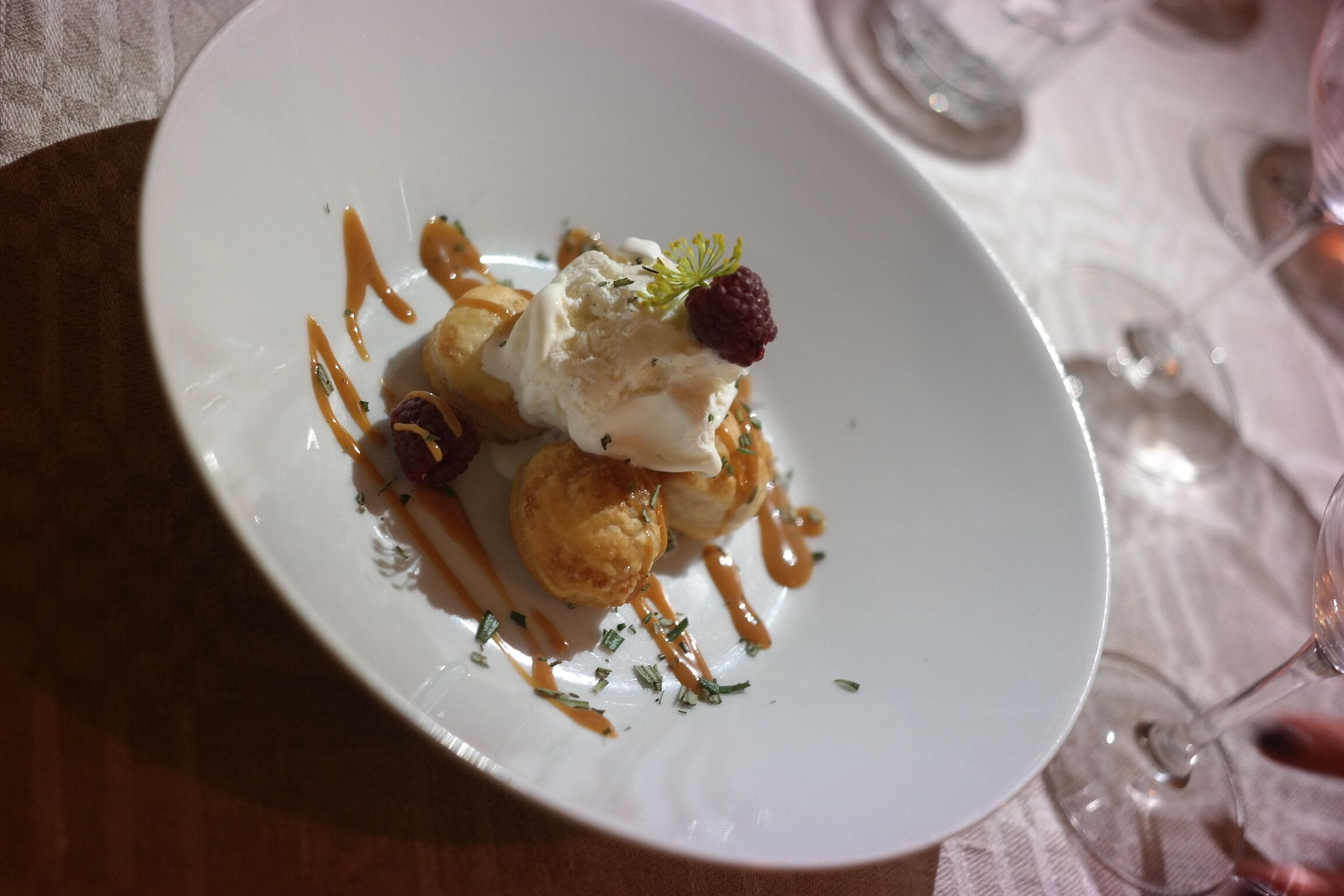 Un plato de postre con una bola de helado, una baya y salsa sobre un plato blanco.