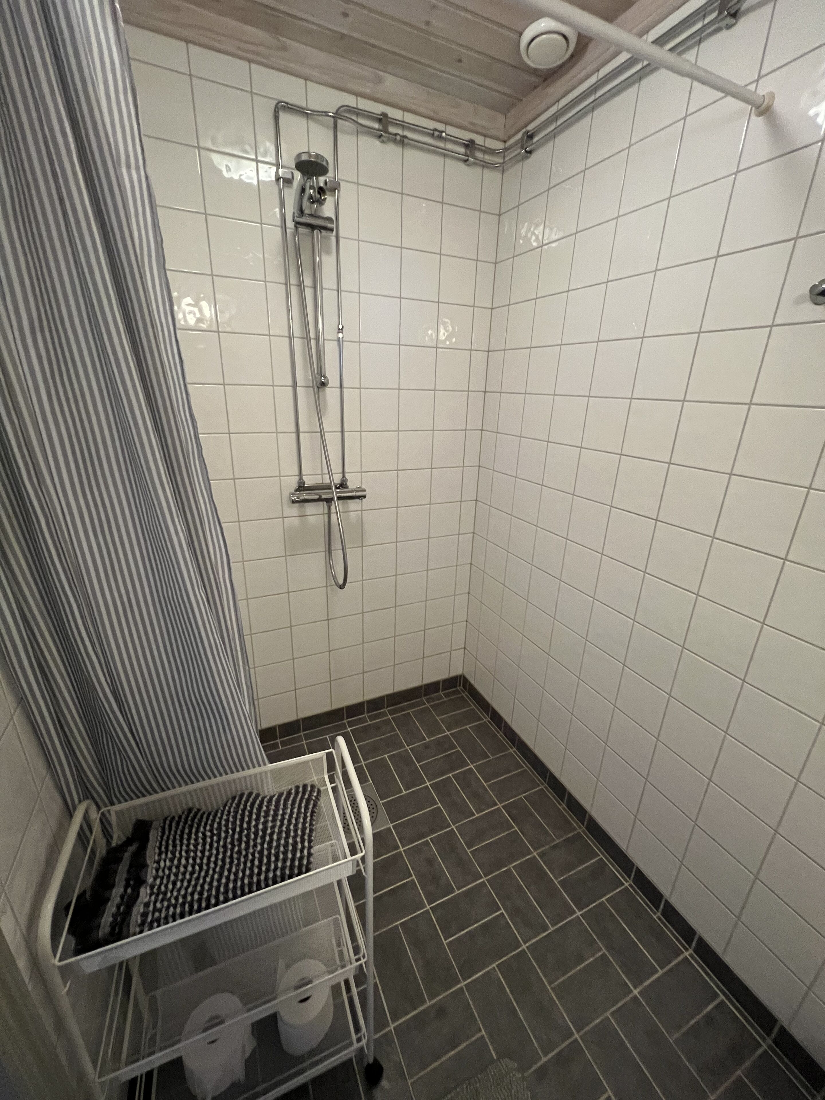A small, tiled shower room with a showerhead, a towel rack, and a rack with toiletries.