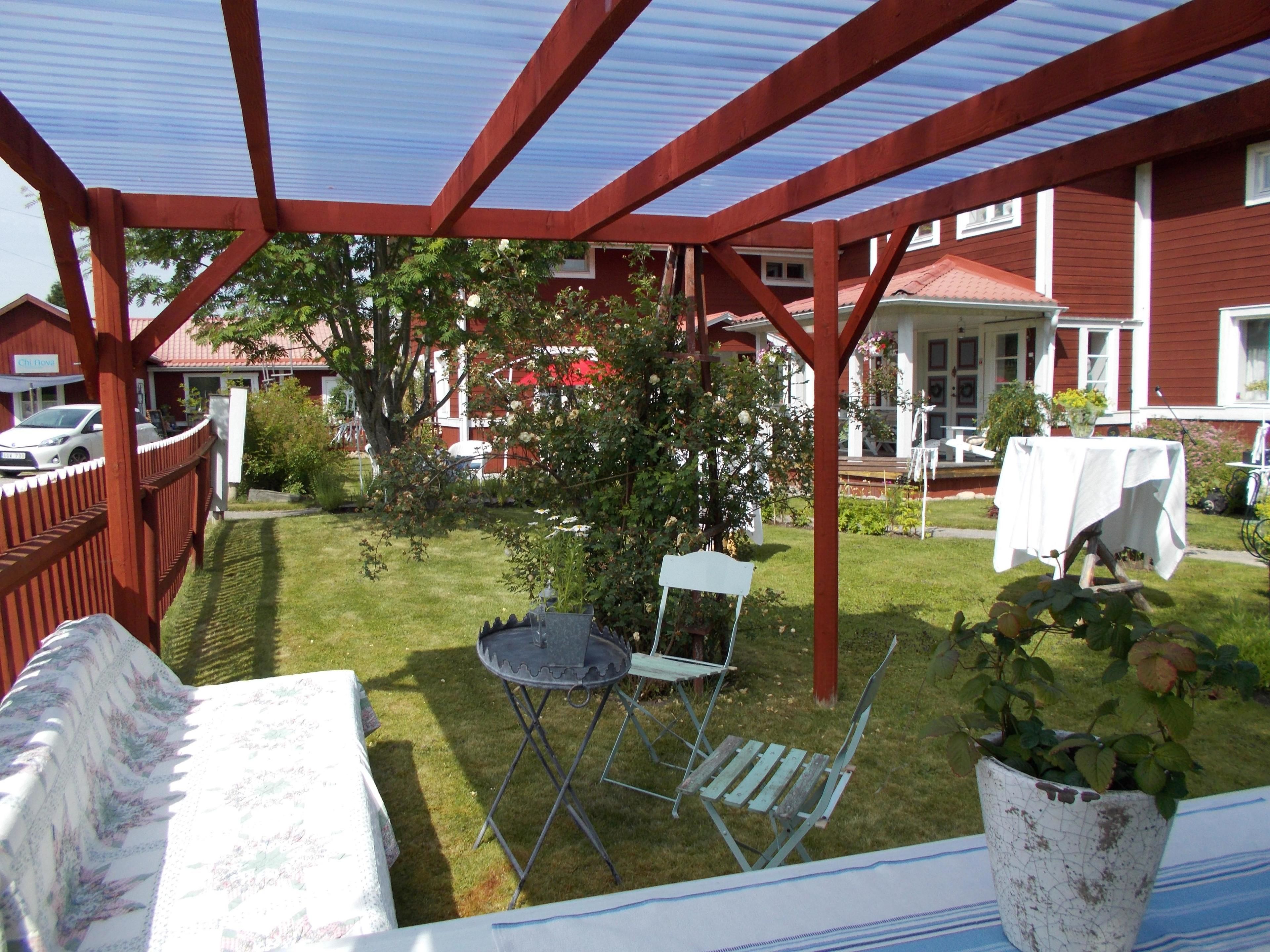 En inglasad uteplats med en röd träram, ett litet bord med ett vitt bordsduksöverdrag, en stol i metall och en krukväxt.