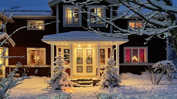 A two-story house with a snow-covered front yard and a lit gazebo. - Chinova Mötesgård (Jarvso)