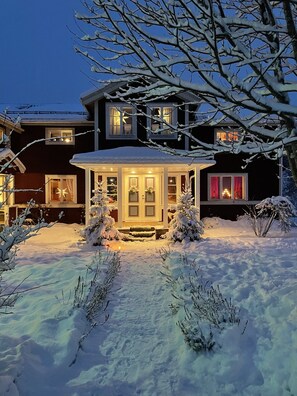 A two-story house with a snow-covered front yard and a lit gazebo. - Chinova Mötesgård (Jarvso)