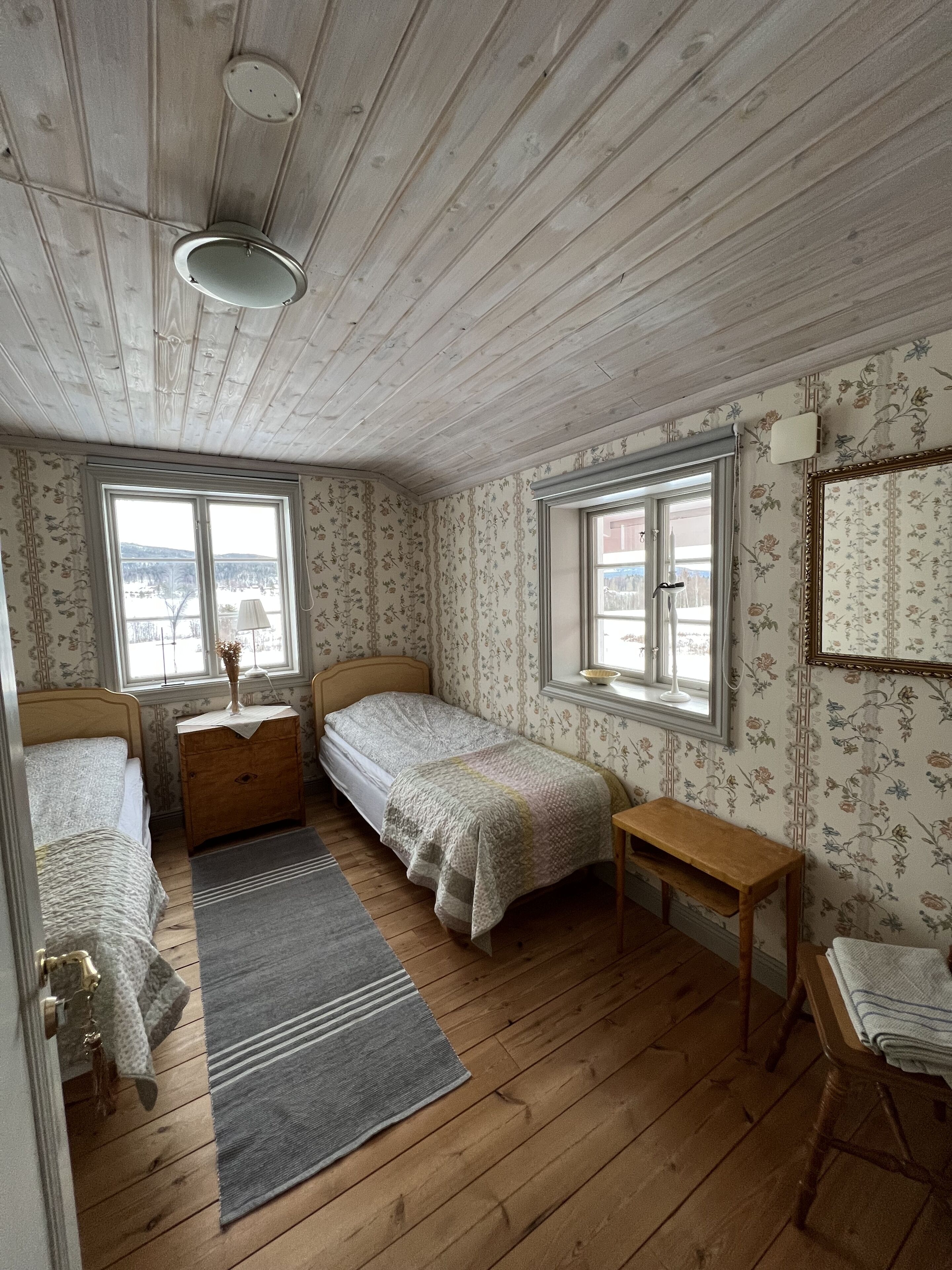 Una habitación con dos camas individuales, un aparador de madera, una mesita y una ventana con vista a un edificio.