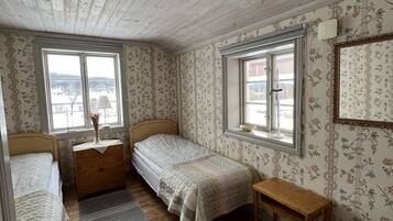 Una habitación con dos camas individuales, un aparador de madera, una mesita y una ventana con vista a un edificio.