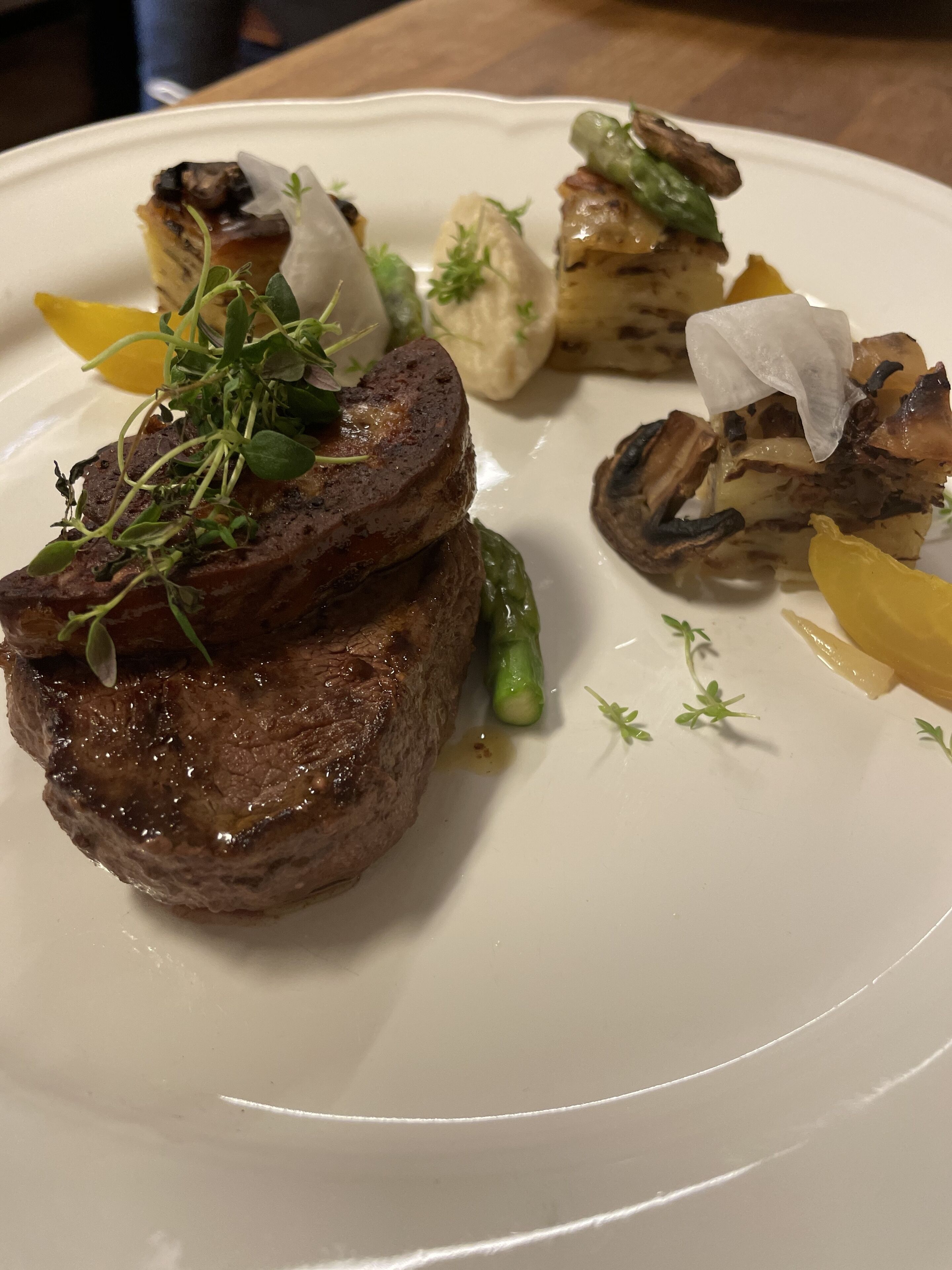 A plate with a steak topped with greens, mushrooms, and a yellow vegetable.