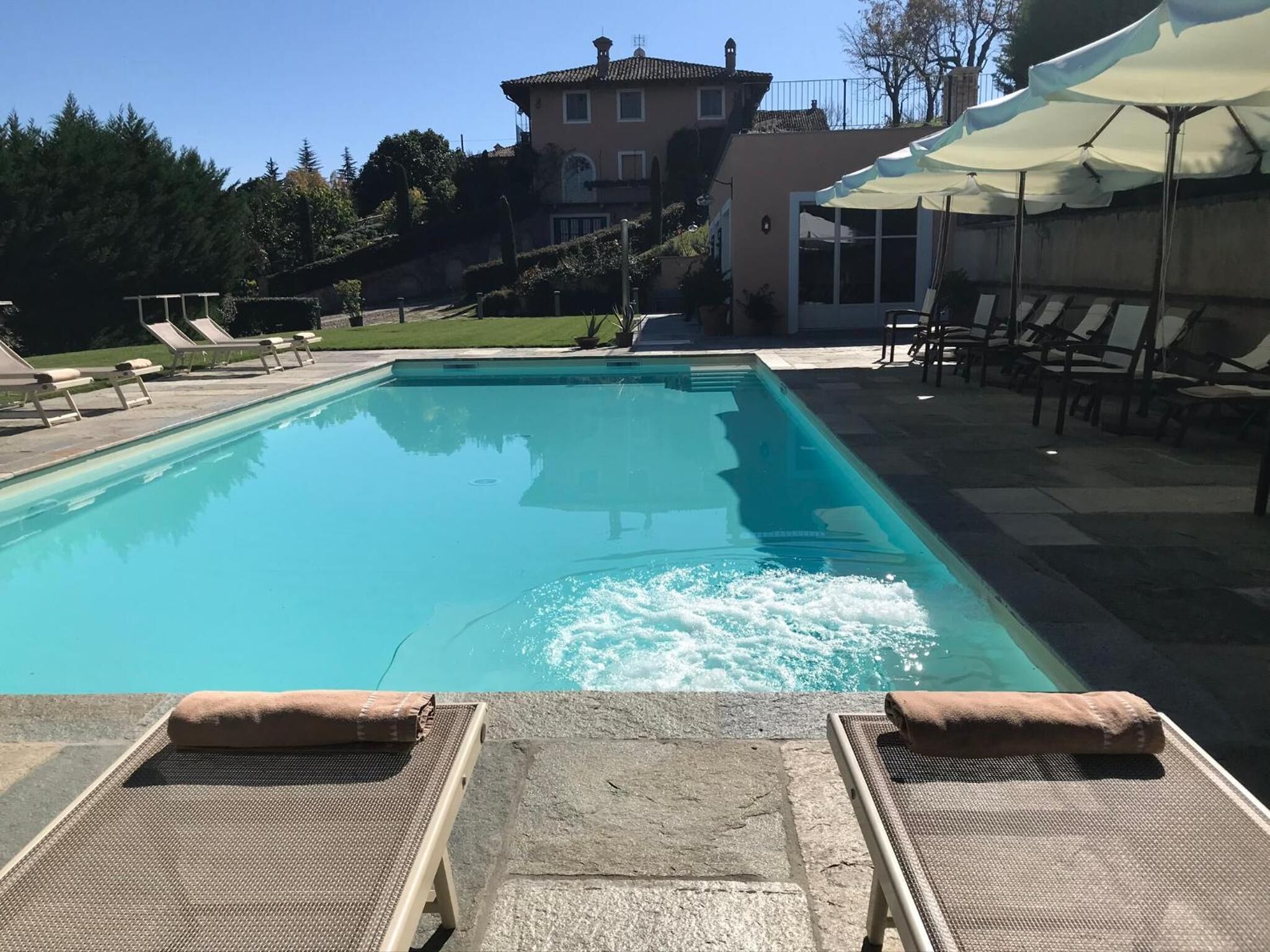 A rectangular swimming pool with clear blue water, surrounded by lounge chairs and umbrellas.