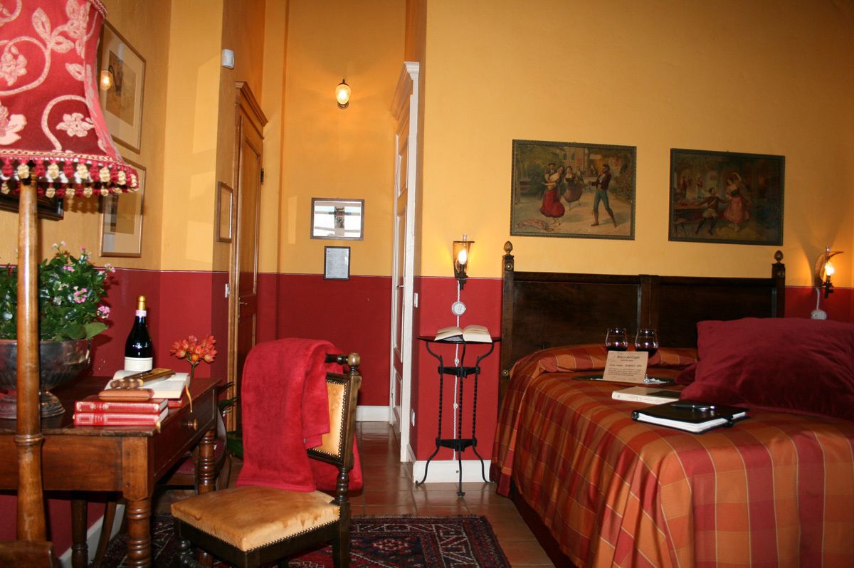 Una camera d'albergo con un letto, una scrivania con una sedia, un comodino con una lampada e un quadro appeso al muro.