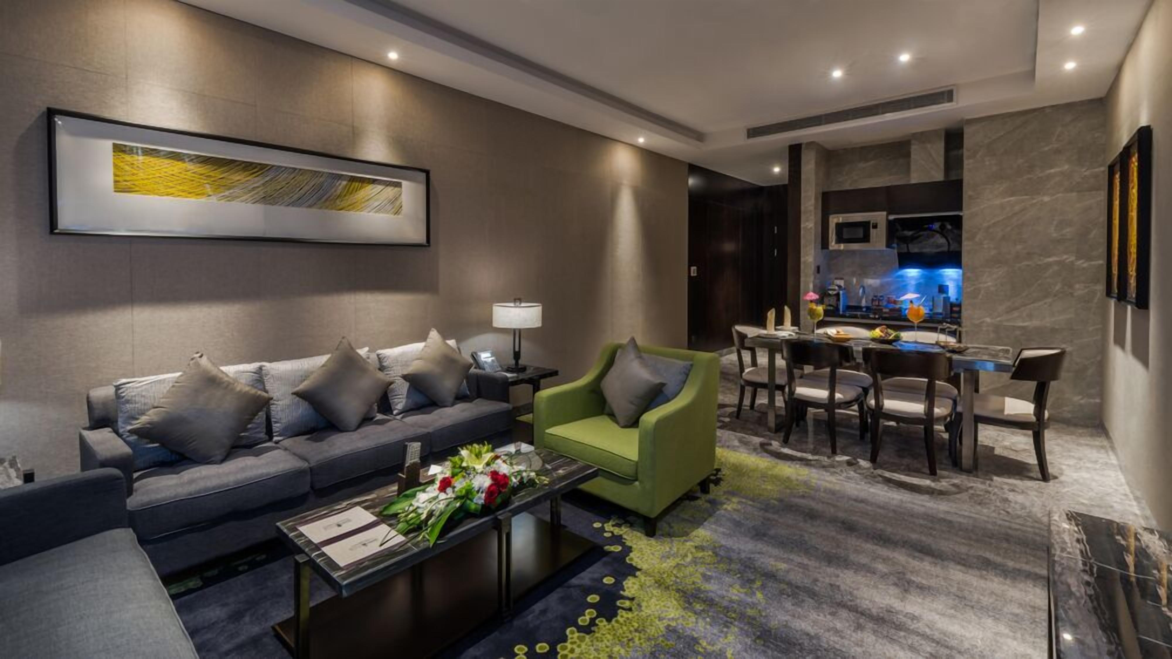 Un salon moderne avec un canapé gris, un fauteuil vert, une table basse ornée de fleurs et un coin repas comprenant une table et des chaises.