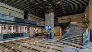 Eine geräumige Lobby mit Marmorboden, einem Empfangstresen, einer Sitzecke und einer Treppe.