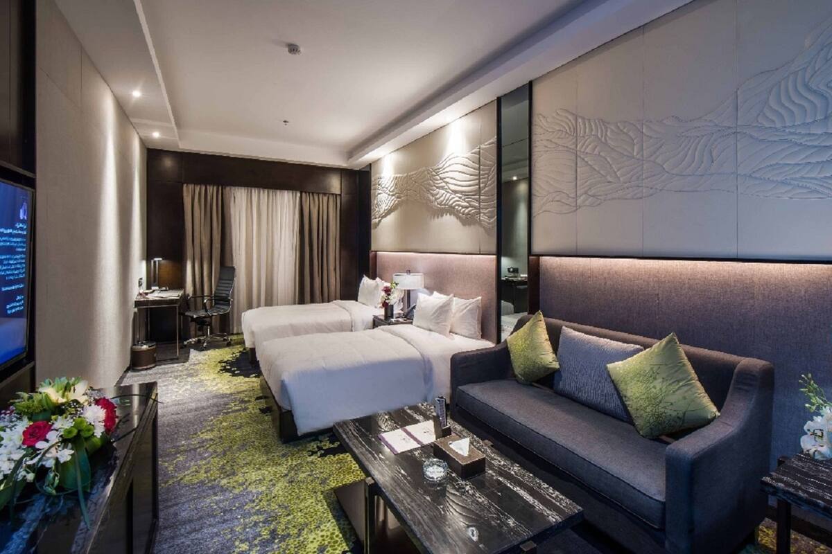 Une chambre d’hôtel comprenant un lit, un canapé, une table basse, un téléviseur et un mur décoratif.