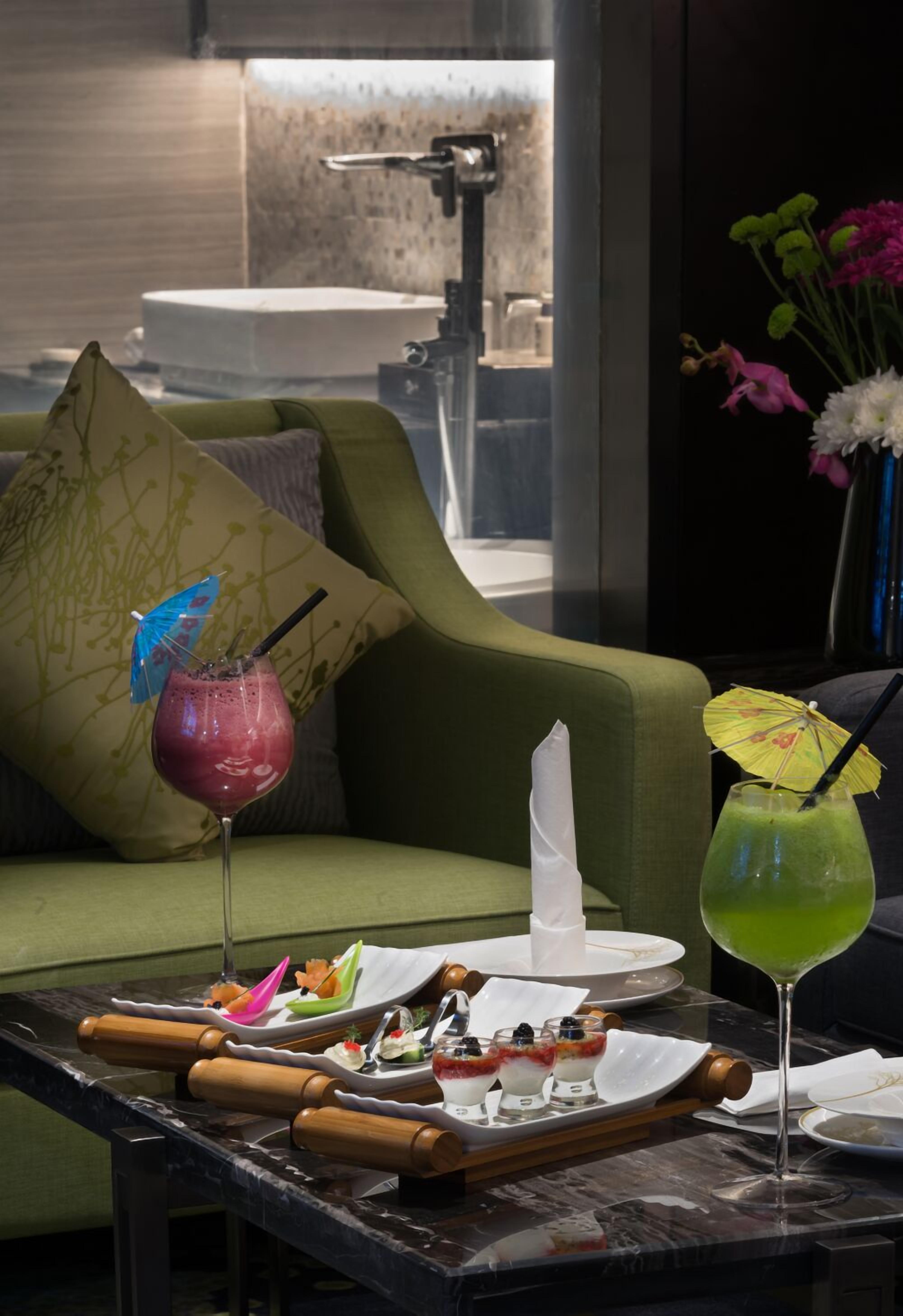 A dining area with a green sofa, a marble table, and a vase with flowers.