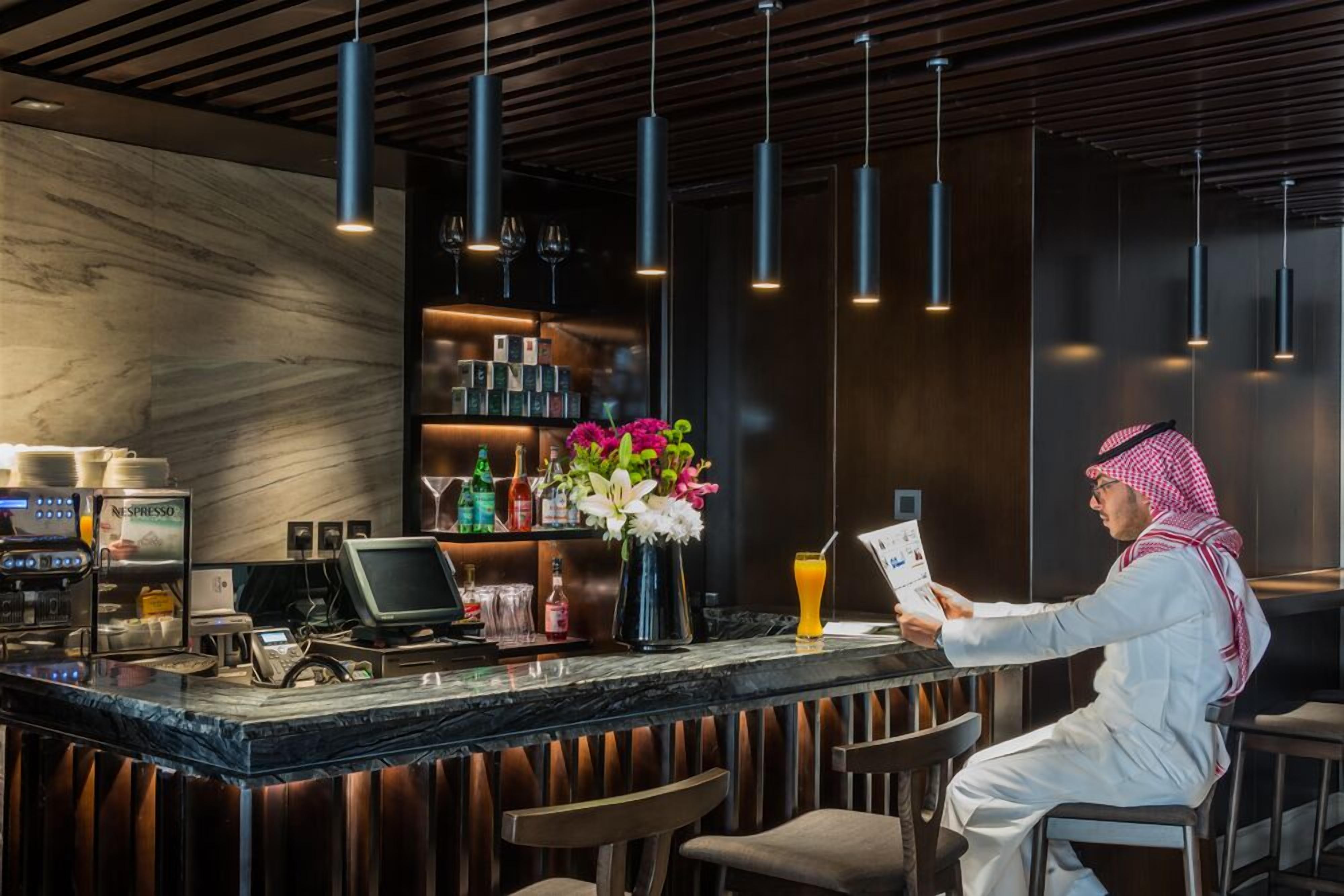 A modern bar area with a marble countertop, espresso machines, and a variety of bottles.