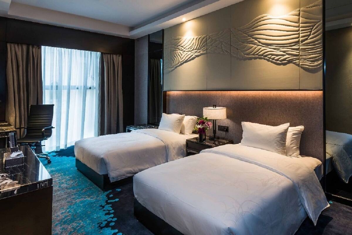 Une chambre d’hôtel avec deux lits, un bureau, une chaise, une lampe et un mur décoratif.