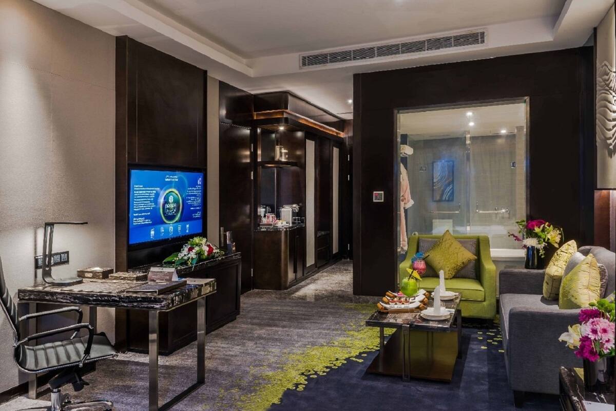 Un hall d’hôtel moderne doté d’un téléviseur à écran plat, d’un comptoir de réception, d’un canapé vert et d’une table basse.