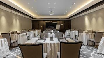 A conference room with multiple tables and chairs, equipped with nameplates, water bottles, and a projector screen.