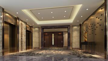 Una hall d'albergo moderna con pavimento in marmo, un ascensore centrale e una parete decorativa con motivi di uccelli.