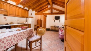 Una cocina rústica con vigas de madera, una mesa de comedor con mantel estampado y un televisor colgado en la pared.