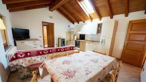 Un comedor acogedor con una mesa preparada para cuatro personas, un televisor sobre un aparador y una cocina al fondo.