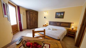 Un dormitorio con cama, un armario de madera, una mesita de noche, una mesa con un cesto de flores y un control remoto.